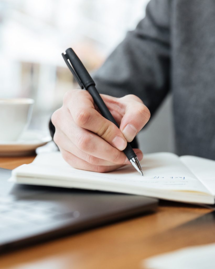 Cropped image of business man sitting by the table in cafe with laptop computer and writing something
